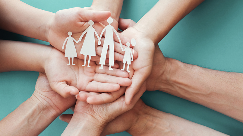 Adult and children hands holding paper family cutout, family hom